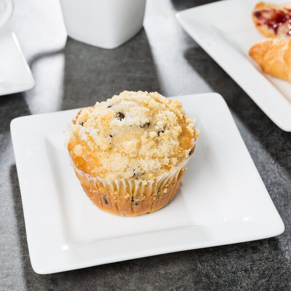 A muffin on a Libbey white square plate next to a cup of coffee.