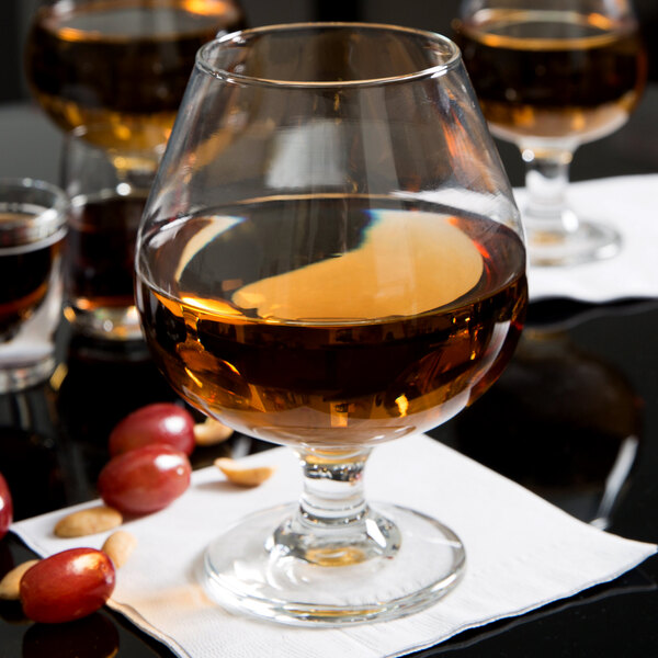 A Libbey brandy glass filled with brown liquid on a table with a bunch of grapes.