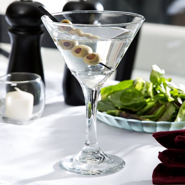 A Libbey martini glass with olives on a table.