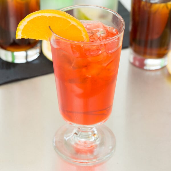 A Libbey footed highball glass filled with a drink, ice, and a slice of orange.