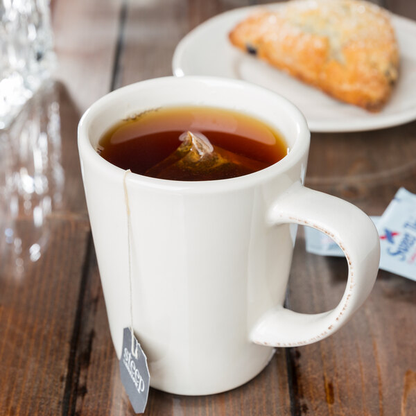 A Libbey cream porcelain mug filled with tea with a tea bag in it on a table.
