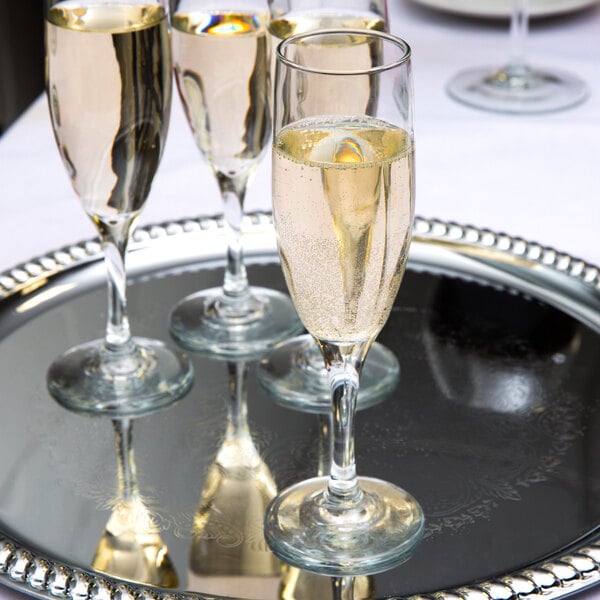 A tray with three Libbey Embassy champagne glasses on it full of champagne.