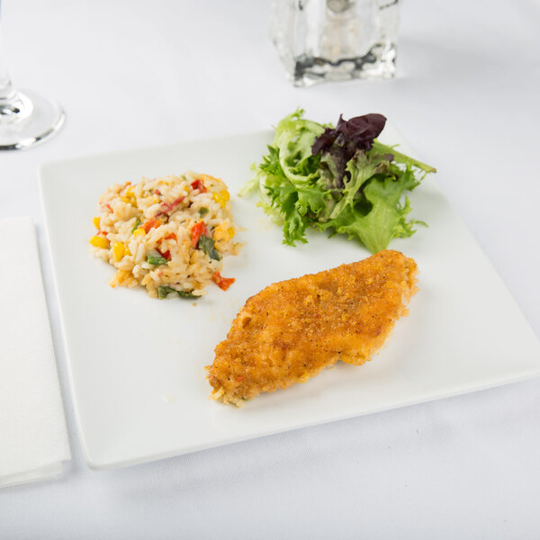 A square white porcelain plate displaying a serving of breaded fish, a portion of rice with vegetables, and a small green salad.