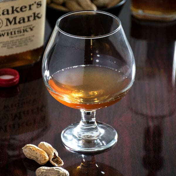 A Libbey brandy glass of liquor and peanuts on a table.