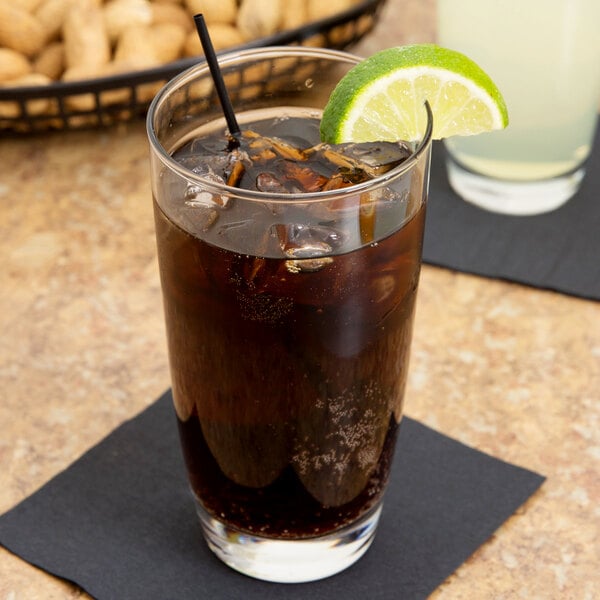 A Libbey cooler glass filled with brown liquid and ice with a lime wedge on the rim.