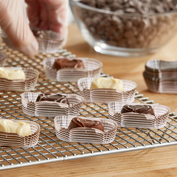 A hand holding a tray of brown oval baking cups filled with chocolate candy.