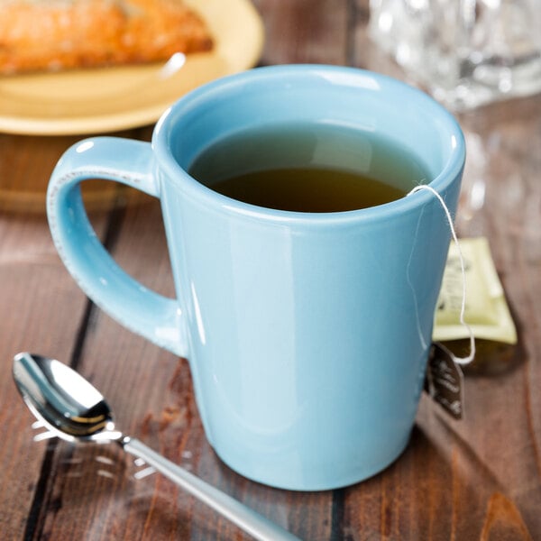 A Libbey blue porcelain mug filled with tea on a wooden table.