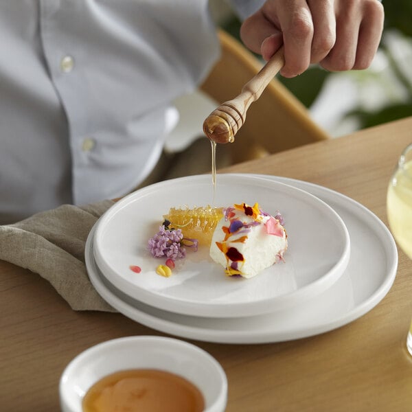 A wooden honey dipper drizzling honey over a Libbey white porcelain plate of food.