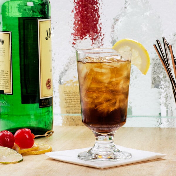 A Libbey footed highball glass with ice tea and lemon on a counter.