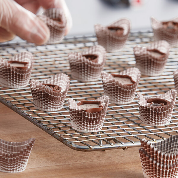 A hand holding a tray of chocolates with brown Novacart boat baking cups.
