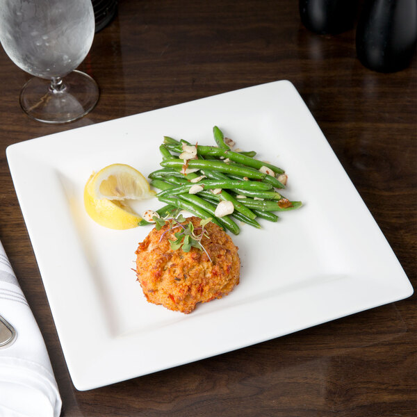 A Libbey Slate Ultra Bright White Wide Rim Square Porcelain Plate with food on it, including a lemon slice.