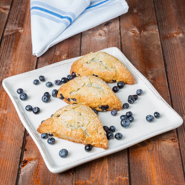 A Libbey square white porcelain tray with blueberry scones and blueberries.