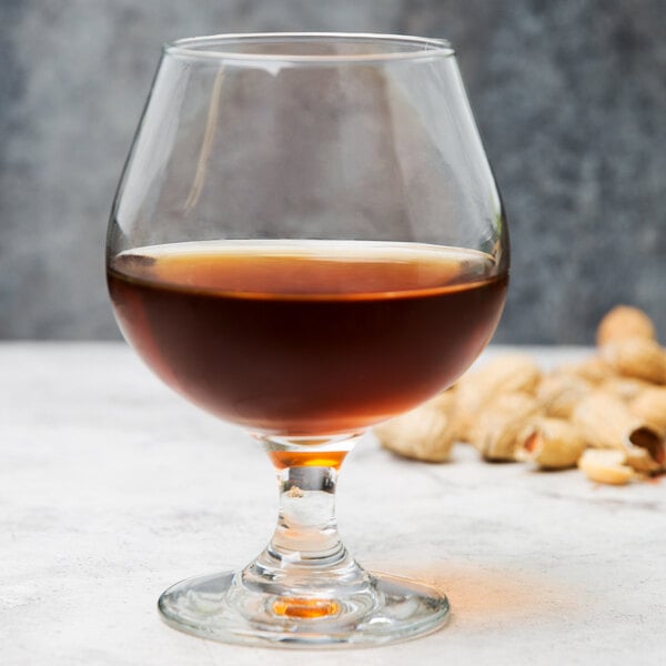 A Libbey Embassy brandy glass filled with dark brown liquid on a table in a bar.