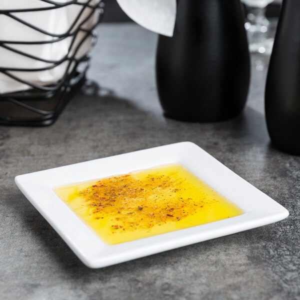 A white square Libbey porcelain plate with a small amount of yellow liquid on it.