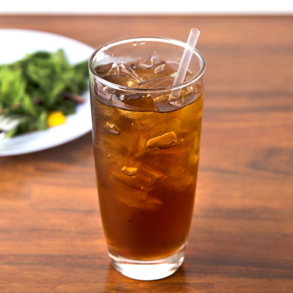 A Libbey cooler glass of iced tea with a straw next to a plate of salad.