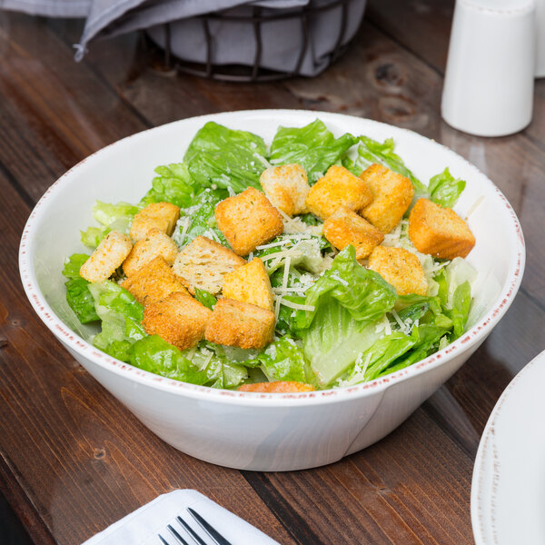 A Libbey round white porcelain serving bowl filled with salad, croutons, and cheese on a table.