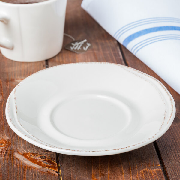 A Libbey Farmhouse cream porcelain saucer on a wooden table with a cup of coffee.