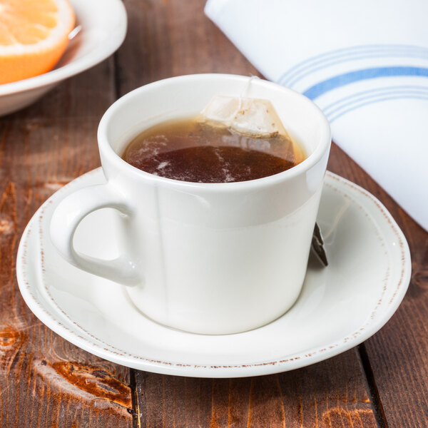A Libbey round cream porcelain saucer with a cup of tea on it, with orange slices.