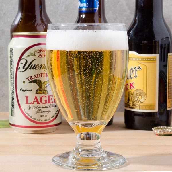 A Libbey Banquet goblet filled with beer next to a bottle of beer.
