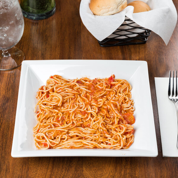 A Libbey Slate Ultra Bright White Wide Rim Square Porcelain pasta bowl filled with spaghetti and sauce on a table.