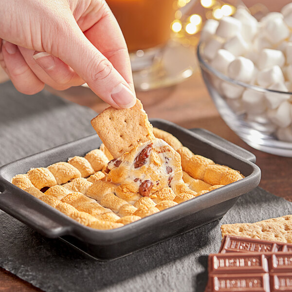 A hand dipping a marshmallow into a bowl of marshmallows.