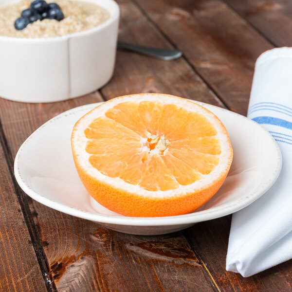 A Libbey round cream porcelain bowl with a grapefruit half and oatmeal with blueberries on a table.