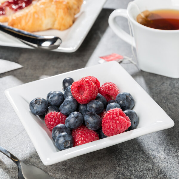 A white square porcelain fruit bowl filled with blueberries and raspberries.