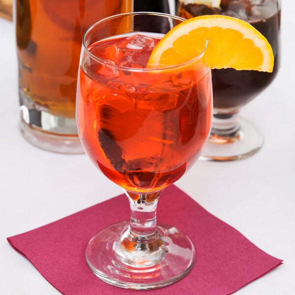 A Libbey Embassy goblet filled with orange liquid and ice with a slice of orange on the rim.