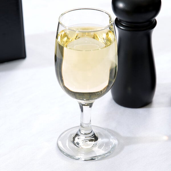 A Libbey white wine glass filled with white wine next to a black salt shaker.