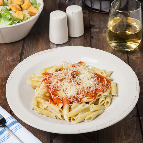 A Libbey round white porcelain pasta bowl with pasta and salad on a table with a glass of white wine.