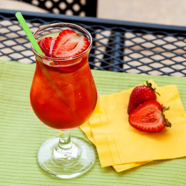 A Libbey Poco Grande glass of red liquid with ice, strawberries, and a straw on a napkin.