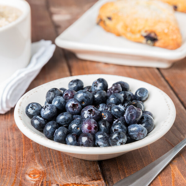 A Libbey round white porcelain bowl filled with blueberries on a table.