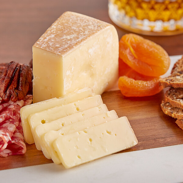 A wedge of Sartori Tennessee Whiskey BellaVitano cheese on a wooden surface with crackers and nuts.