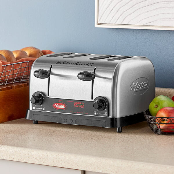 A Hatco commercial toaster on a kitchen counter with a metal basket of green and red apples on top.