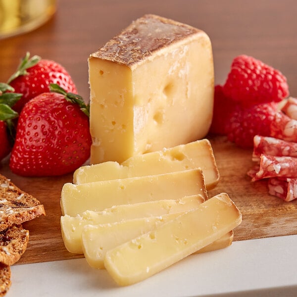 A close-up of Sartori Balsamic BellaVitano cheese slices on a wooden board with strawberries.