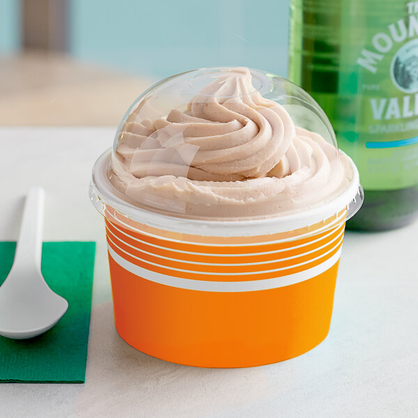 A close up of a Choice orange paper frozen yogurt cup with a plastic lid filled with ice cream.