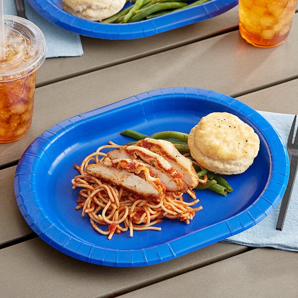 A table with a plate of food and a Creative Converting cobalt blue oval paper platter with green beans on it.