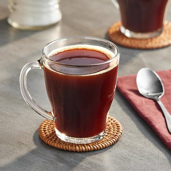 A glass mug of Maxwell House decaf coffee on a coaster with a spoon.