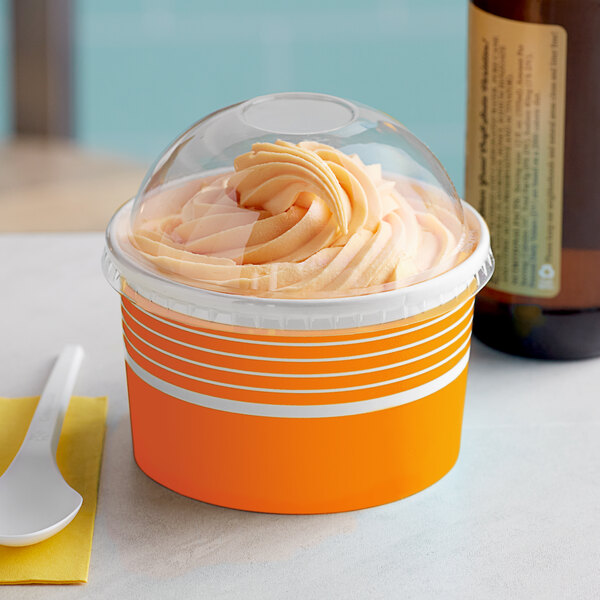 A Choice orange paper frozen yogurt cup with a plastic lid full of orange frozen yogurt on a yellow surface.