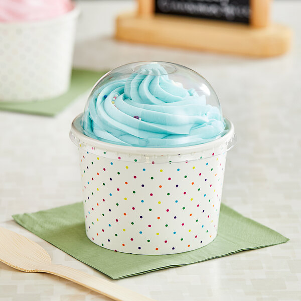 A Choice paper cup with a blue and white polka dot design filled with frozen yogurt and topped with a plastic lid.