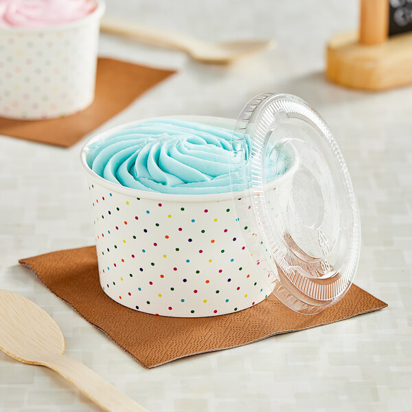 Two polka dot paper cups with frozen yogurt and wooden spoons on a table.