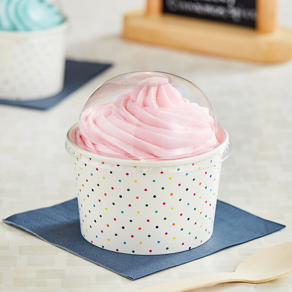Two polka dot paper cups of frozen yogurt with dome lids on a table.