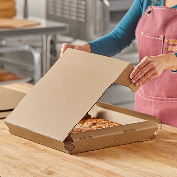 A woman opening a Choice Kraft corrugated pizza box on a table.