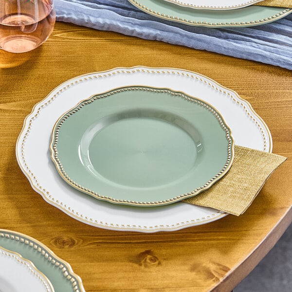 A Visions Eucalyptus plastic plate with gold trim on a table set with wine glasses.