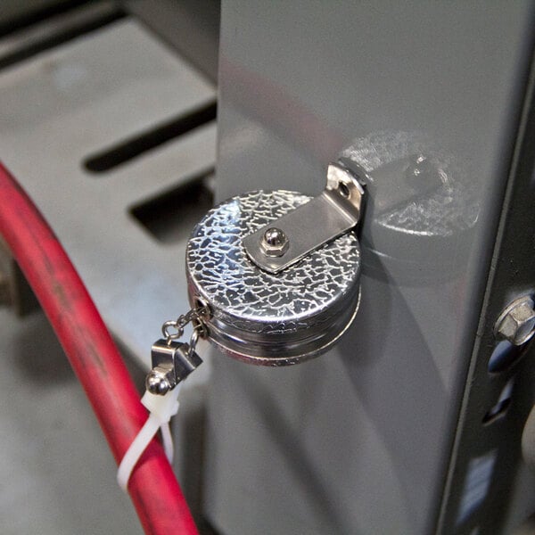 A chrome-plated metal box with two round metal objects attached to a metal surface by red cables.