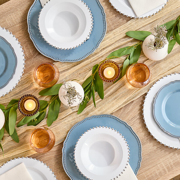 A table set with white Visions plastic plates with silver beaded rims and glasses.
