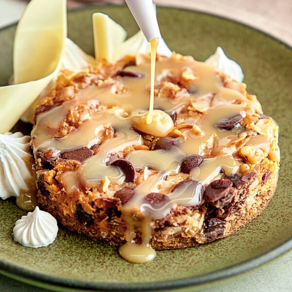 A piece of cake drizzled with Monin White Chocolate Flavoring Sauce on a plate.
