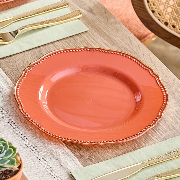 A Visions Terra Cotta plastic plate with a gold vintage rim on a table with other plates and utensils.