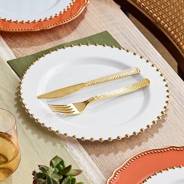 A Visions white plastic plate with a gold beaded rim, a fork and knife on it.
