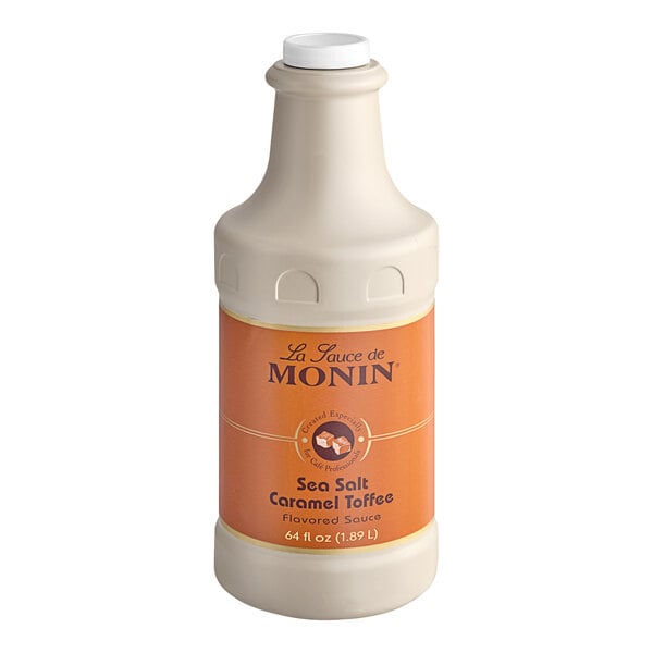 A white Monin bottle of Sea Salt Caramel Toffee Flavoring Sauce with an orange label and lid.